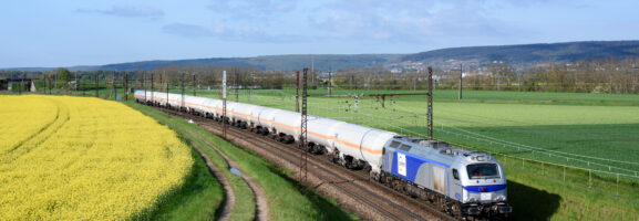 Train de fret circulant à travers des paysages agricoles, longeant un champ de colza en fleurs