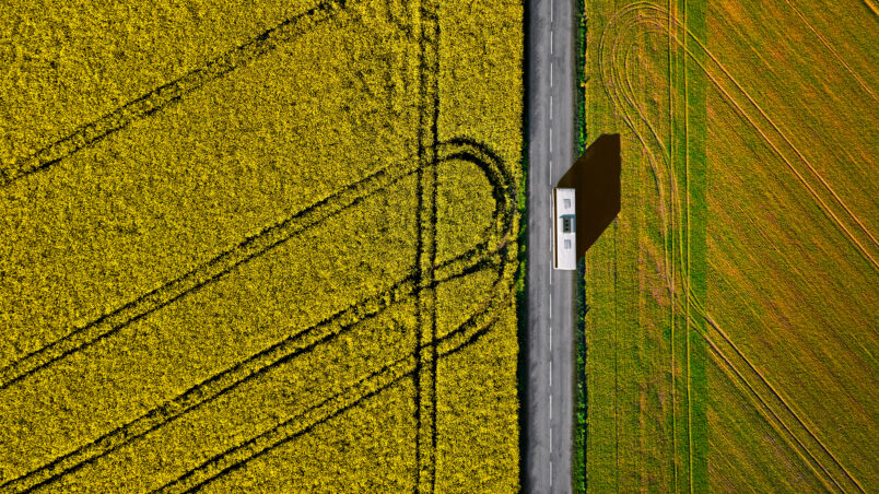 Bus roulant sur une route bordée de champs de colza vus du ciel
